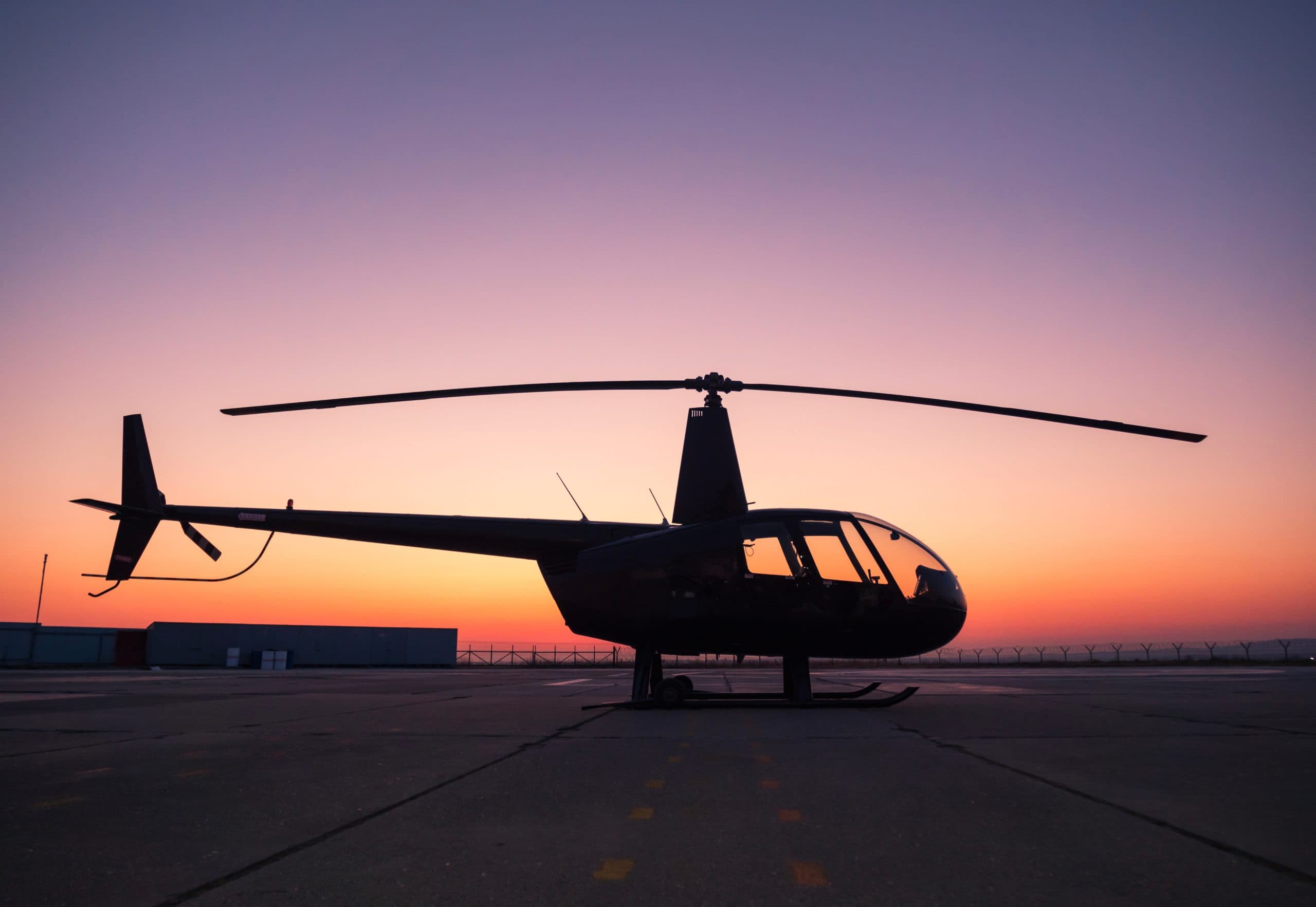 A,Black,Helicopter,Is,Sitting,On,The,Ground,At,Sunset.